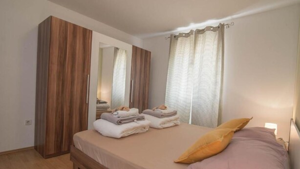 A bedroom with a bed, a wooden wardrobe, a mirror, and a window with curtains. - Veli Lošinj Hilltop Oasis (Mali Losinj)
