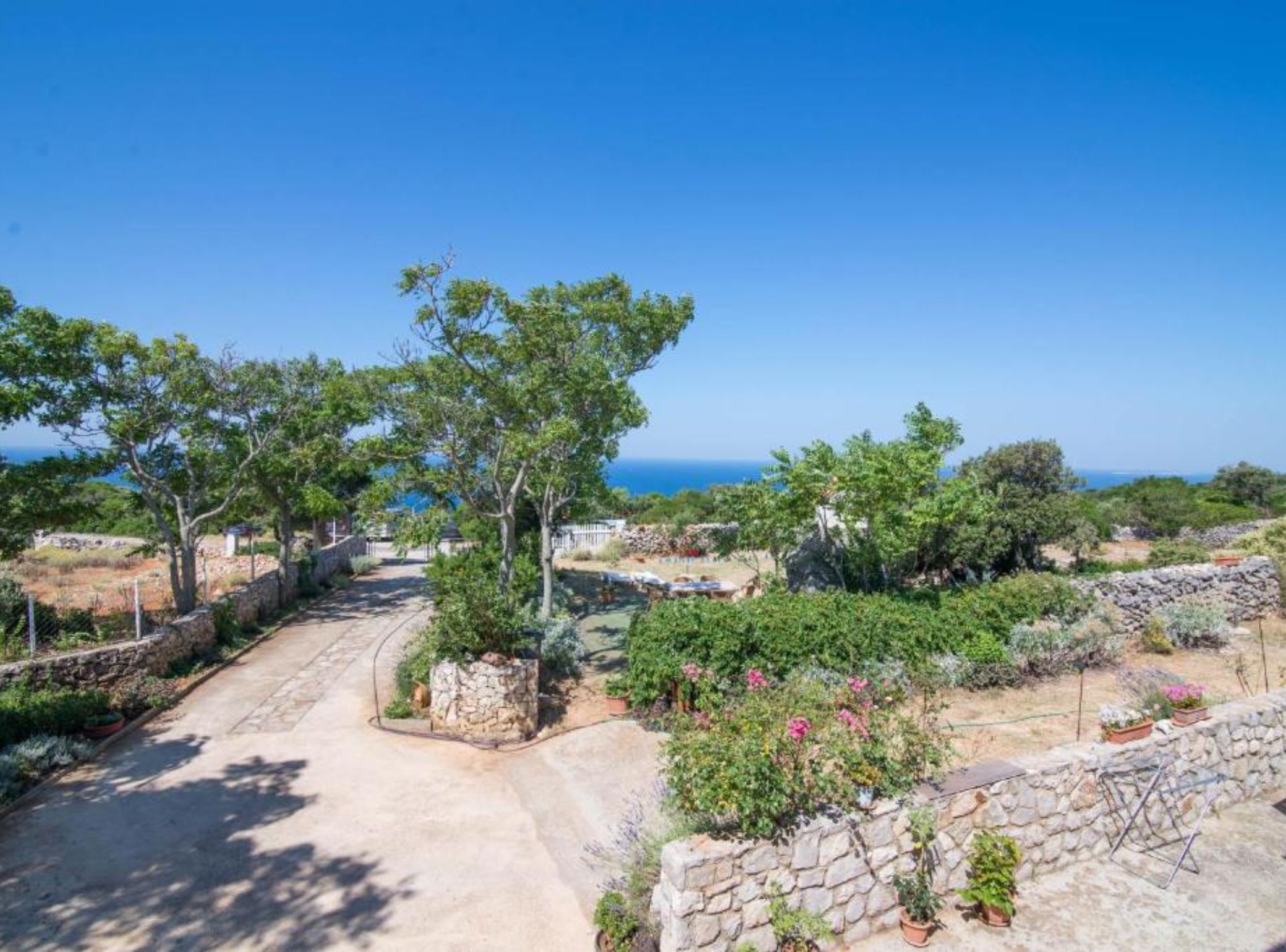 A pathway leading to a stone wall with potted plants and a view of the sea.