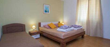 A double bed with a wooden headboard, a nightstand with a lamp, and a window with curtains.
