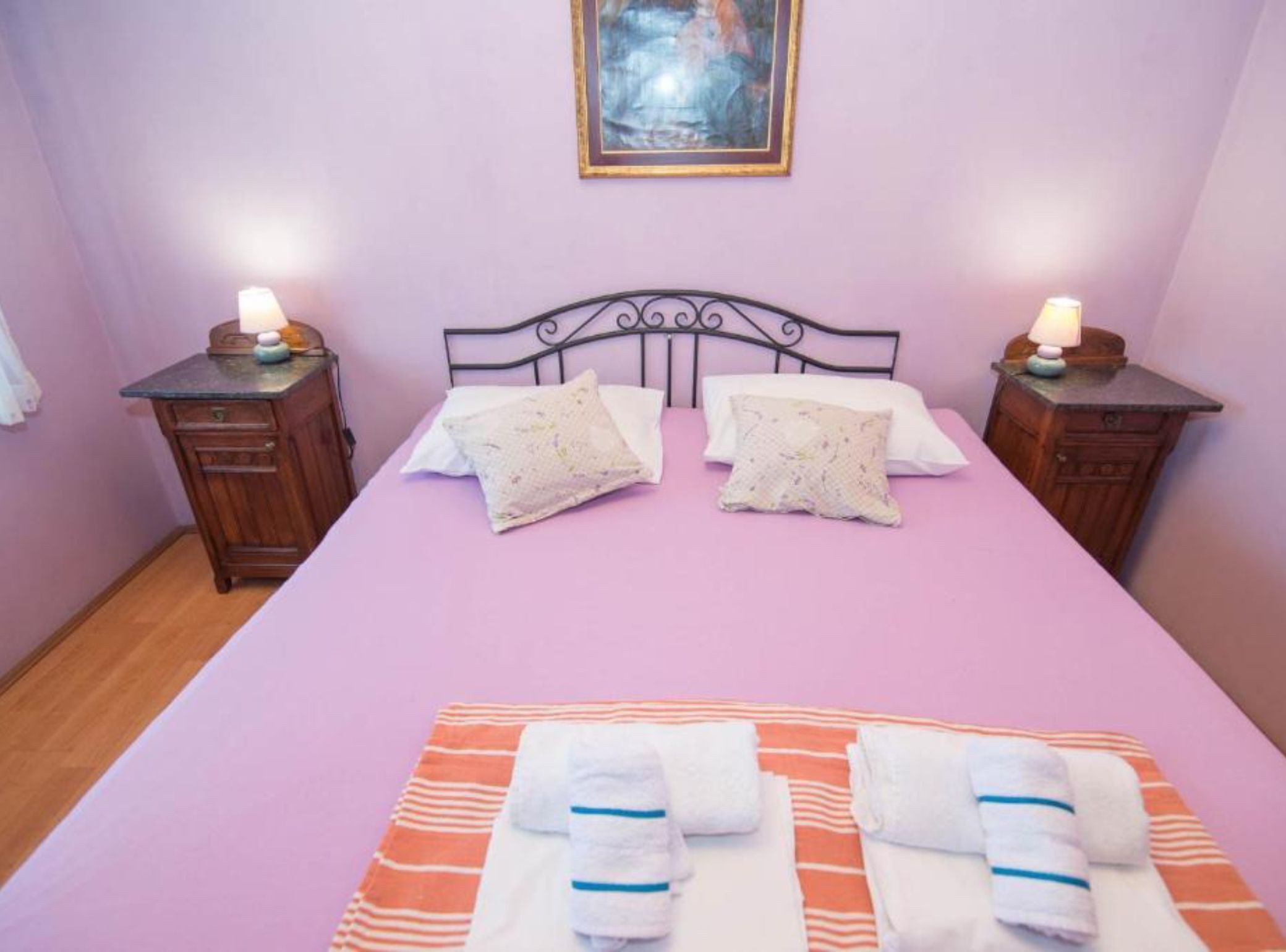 A bedroom with a bed, two nightstands, a painting on the wall, and a window.