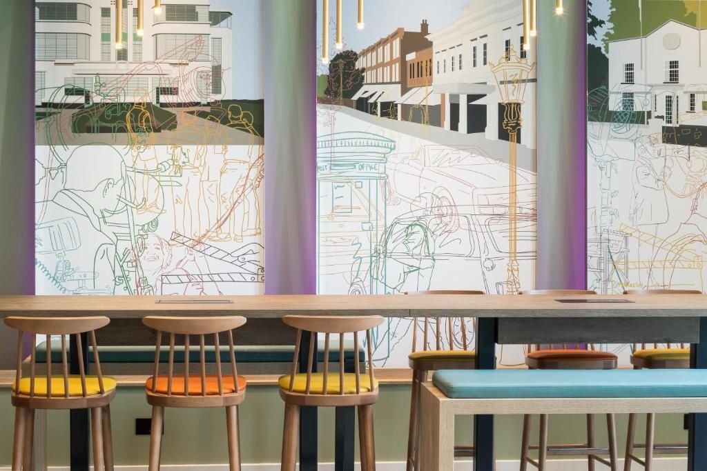 Un bar con taburetes de madera y un banco, con vistas a una calle a través de grandes ventanales.