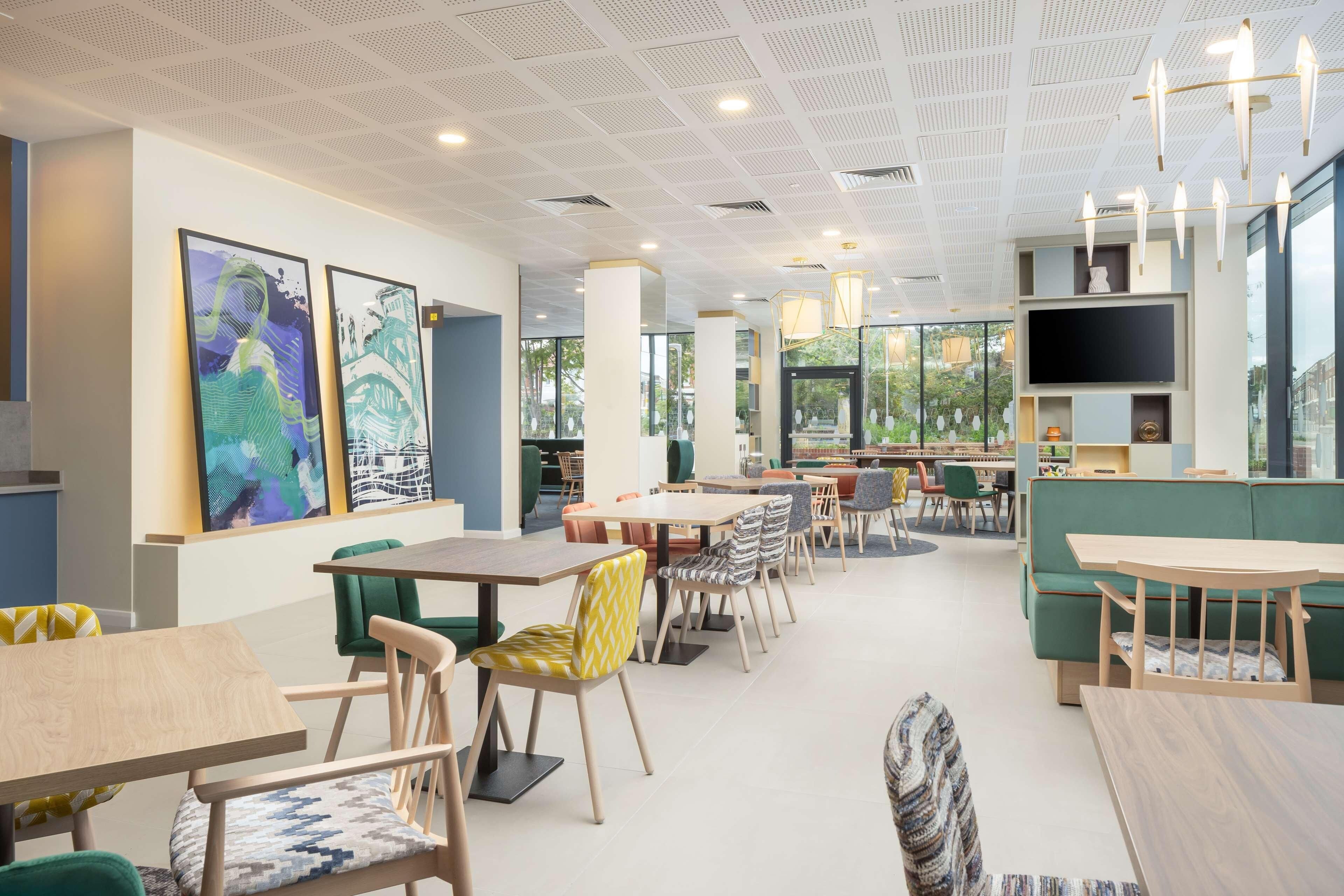 A modern dining area with tables and chairs, a large TV screen, and artwork on the walls.