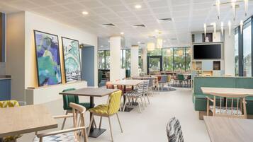 A modern dining area with tables and chairs, a large TV screen, and artwork on the walls.