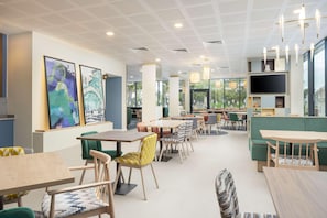 A modern dining area with tables and chairs, a large TV screen, and artwork on the walls. - Hampton By Hilton Nuneaton (Nuneaton)