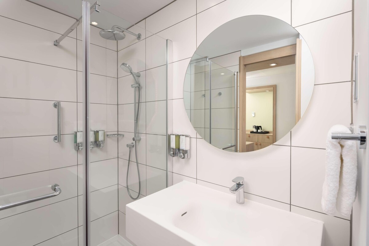 A modern bathroom with a glass-enclosed shower, a white sink, and a large mirror.