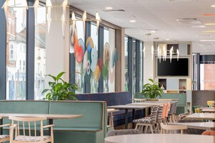 Un restaurante moderno con asientos tapizados en verde, mesas de madera y plantas en macetas.