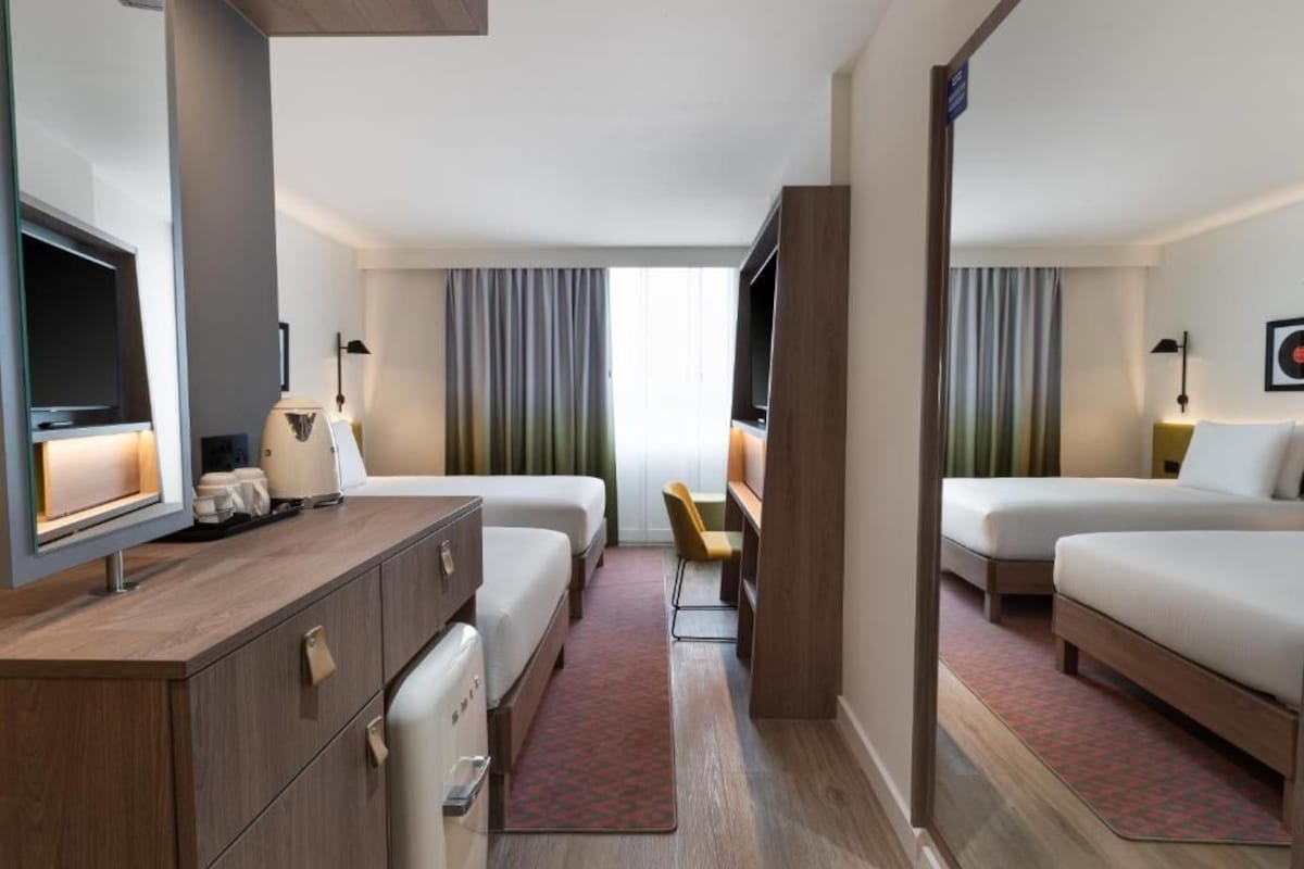 A hotel room with two beds, a desk, a TV, and a small seating area.