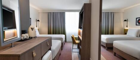 Ein Hotelzimmer mit zwei Betten, einem Schreibtisch, einem Fernseher und einer kleinen Sitzecke.