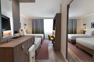 Habitación de hotel con dos camas, un escritorio, un televisor y una pequeña zona de estar.