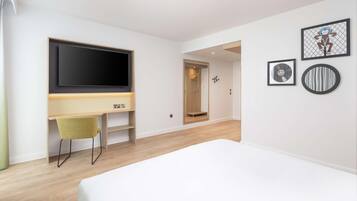 A modern bedroom with a large bed, a desk with a chair, a TV, and a shower area.