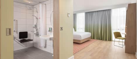 A modern hotel room with a shower, a bed, a TV, and a window with curtains.