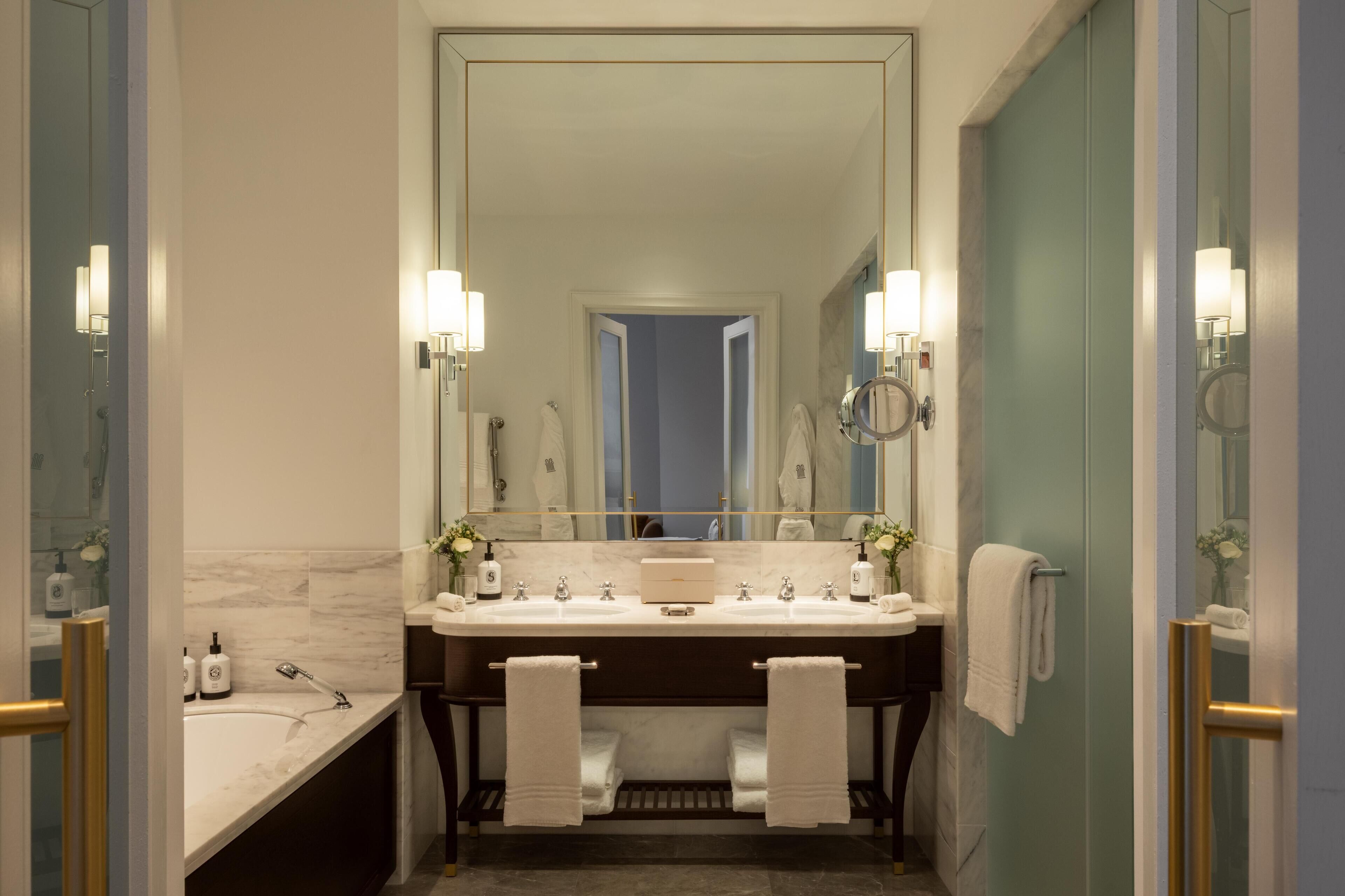 Een moderne badkamer met een grote spiegel, twee wasbakken en een bad.