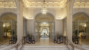 Un vaste hall d’entrée avec des marches en marbre, un lustre et des portes en verre disposées de manière symétrique.