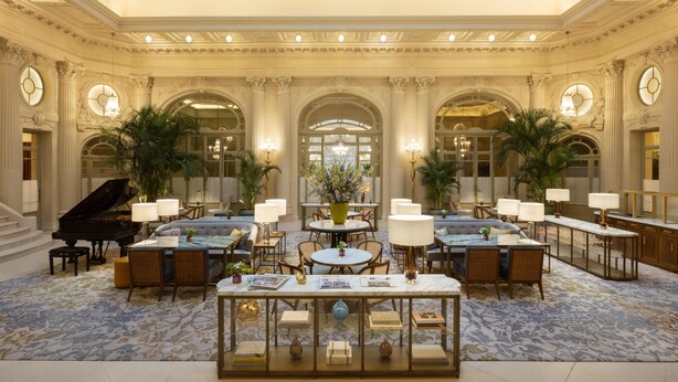 Un vaste hall d’entrée avec un plafond haut, des colonnes richement décorées, un piano à queue et un espace de détente central agrémenté de tables et de chaises.