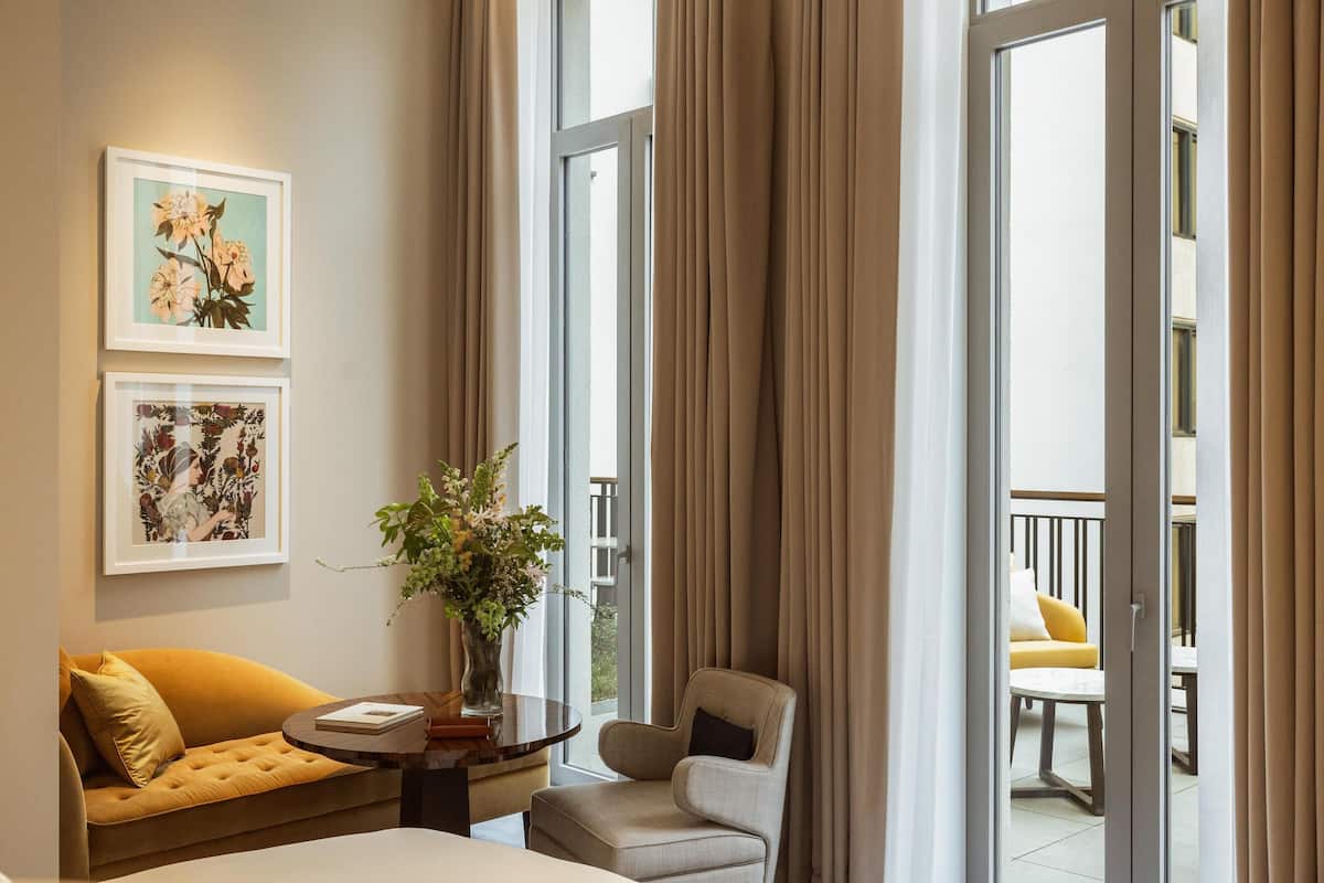 Ett modernt hotellrum med en soffa, en fåtölj och ett bord med en vas med blommor.