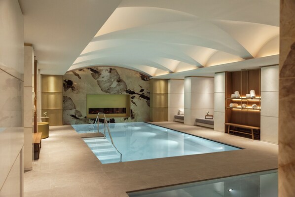 Une piscine intérieure moderne avec un mur en marbre, un banc et un écran de télévision.