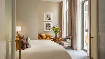 A hotel room with a large bed, a sofa, a chair, a small table, and a potted plant.