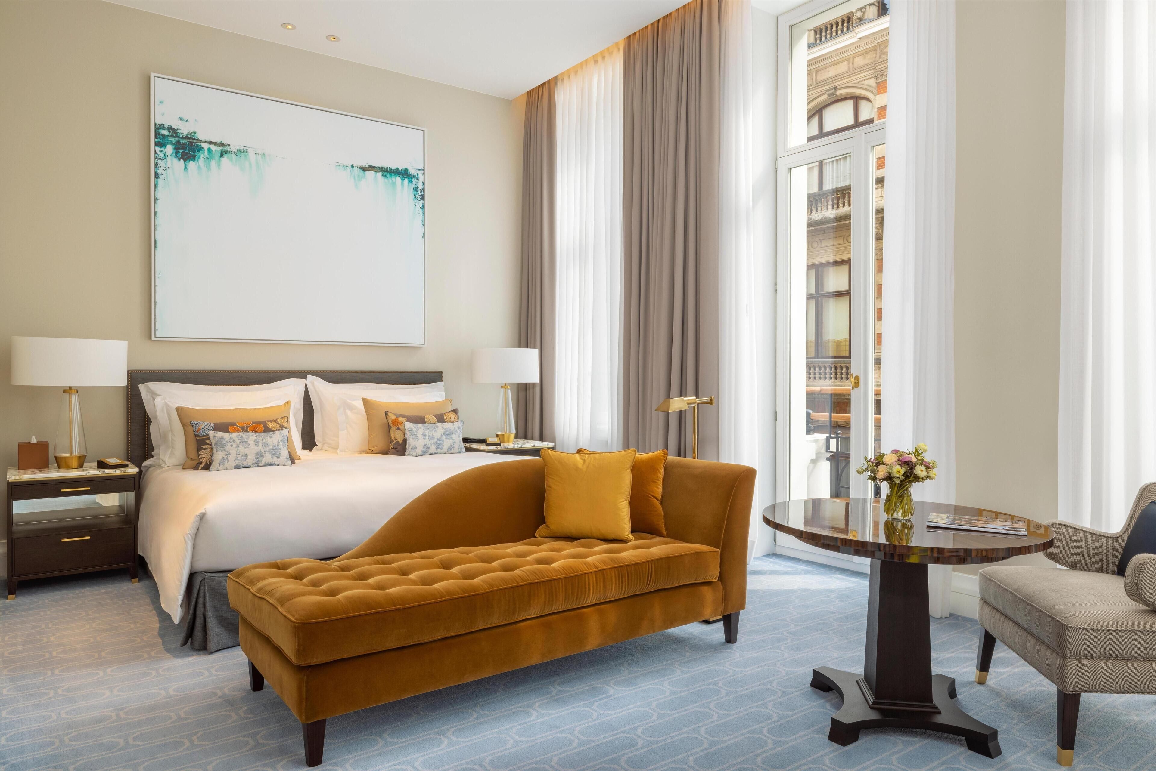 A hotel room with a large bed, a sofa, a round table, and a large window with curtains.
