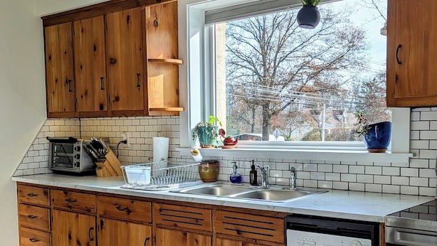 A kitchen with wooden cabinets, a built-in oven, a dishwasher, and a window with a view of trees.