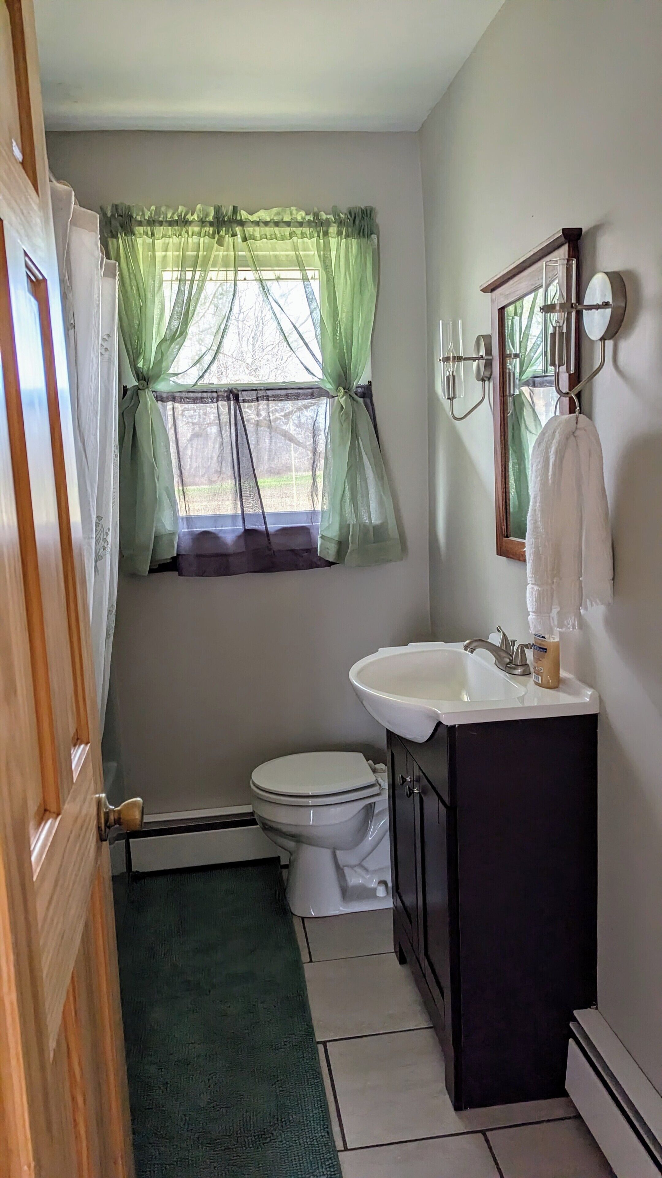 A bathroom with a toilet, sink, and green curtains.