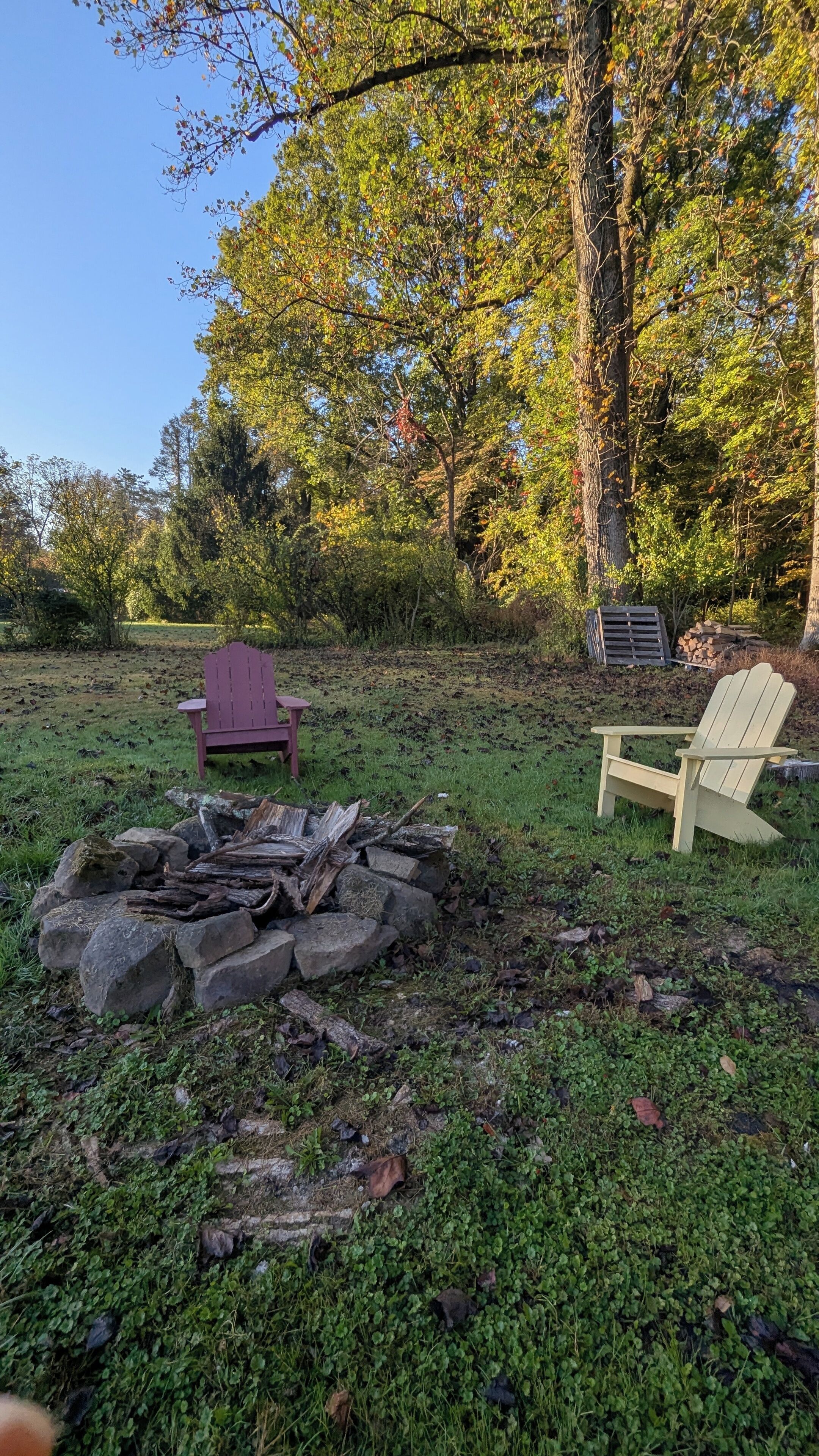A backyard with two Adirondack chairs, a fire pit, and a stack of firewood.