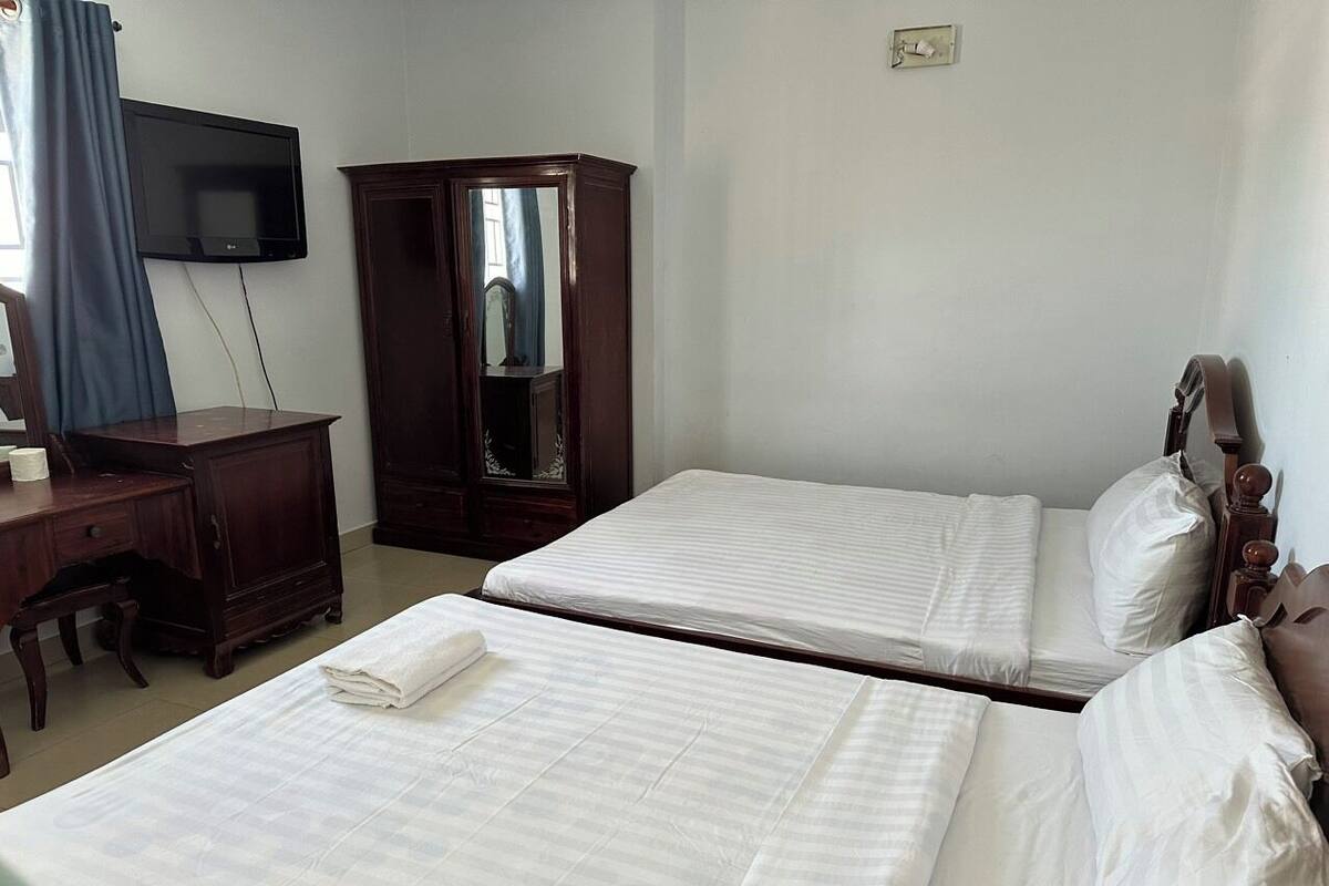 Une chambre d’hôtel avec deux lits, un bureau, une armoire et un téléviseur.