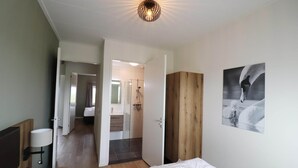 A hotel room with a bed, a bedside table, a lamp, a wooden wardrobe, and a bathroom visible through an open door. - Villa in Leons near Frisian Lake District (Leons)