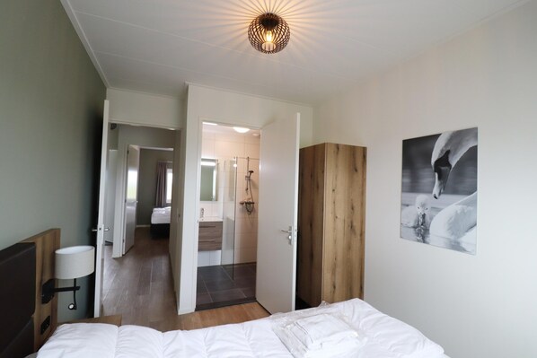 Ein Hotelzimmer mit Bett, Nachttisch, Lampe, einem Holzschrank und einem durchgegangenen Tür sichtbaren Badezimmer.
