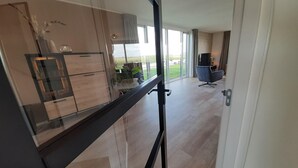A modern kitchen with a glass partition, a dining area with a table and chairs, and a view of the outdoors. - Villa in Leons near Frisian Lake District (Leons)