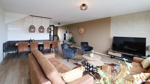 A modern living room with a sofa, chairs, a dining area, and a TV. - Villa in Leons near Frisian Lake District (Leons)