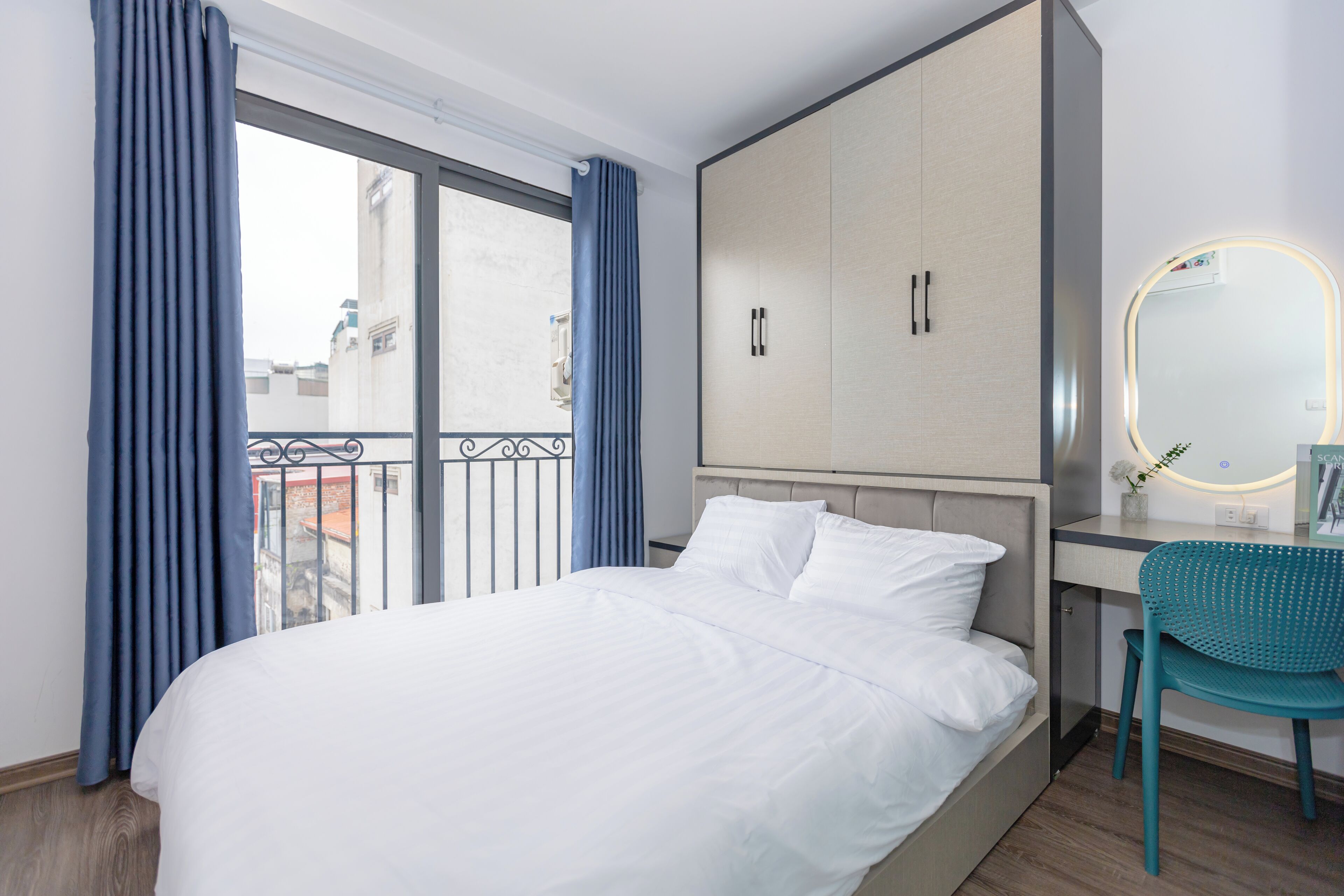 A hotel room with a bed, a desk, a chair, a wardrobe, and a balcony with curtains.