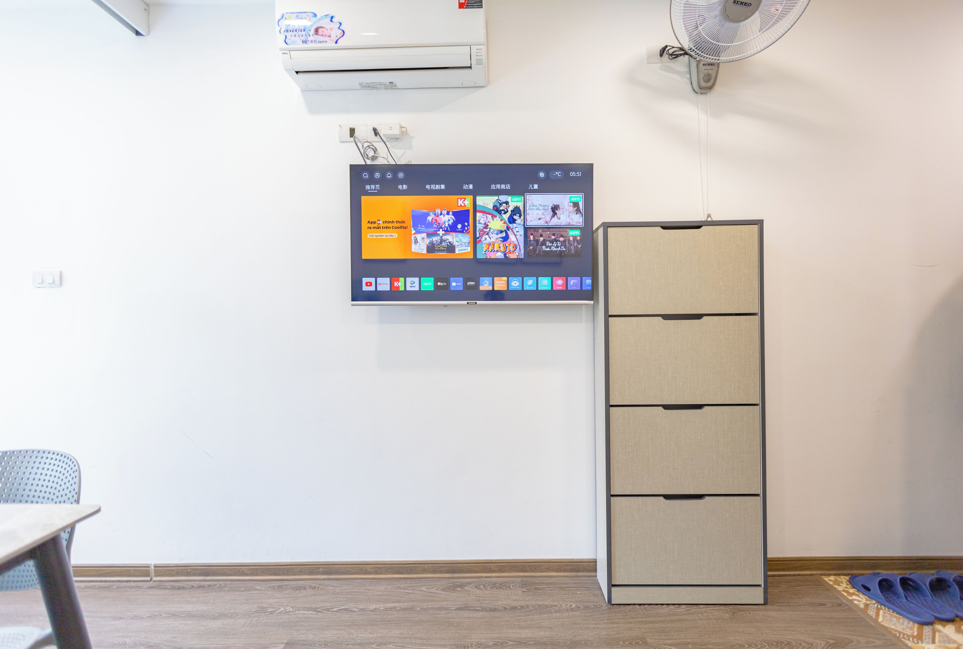 Ein Zimmer mit einem an der Wand befestigten Flachbildfernseher, einem Schrank und einem Paar Hausschuhen auf dem Boden.
