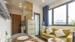 Kompakti hotellihuone, jossa on ruokailutila, sohva ja suuri ikkuna, josta avautuu näkymä kaupunkimaisemaan.