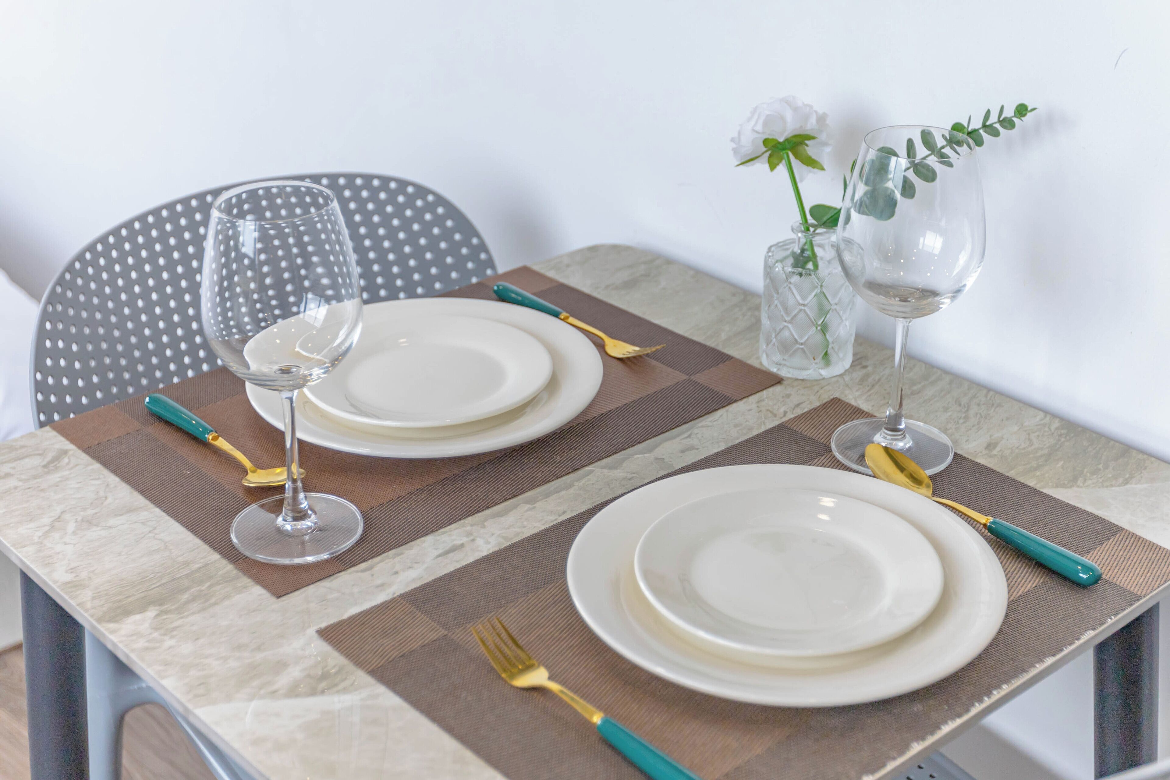 A dining table set with plates, cutlery, and glasses, accompanied by a chair and a vase with flowers.