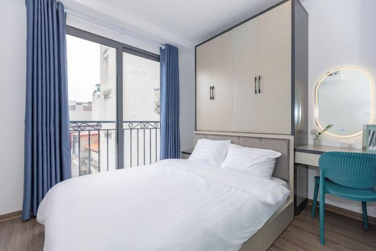 A hotel room with a bed, a desk, a chair, a wardrobe, and a balcony with curtains.