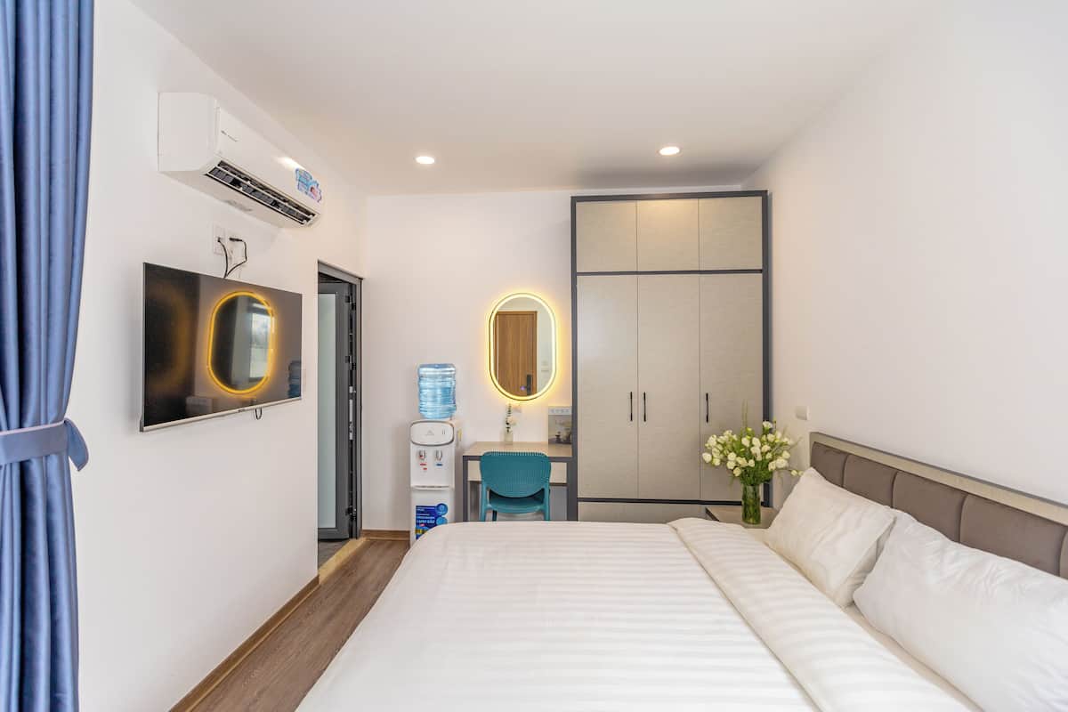 A hotel room with a bed, a desk with a chair, a water dispenser, a mirror, and a wardrobe.