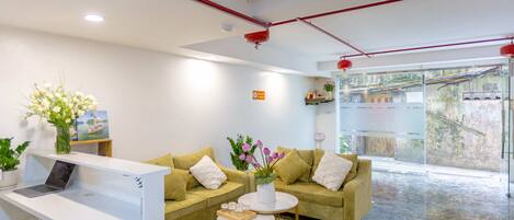 A modern reception area with a white desk, two sofas, and a coffee table. There is a laptop on the desk, and the room has a large window with a view of the outside.