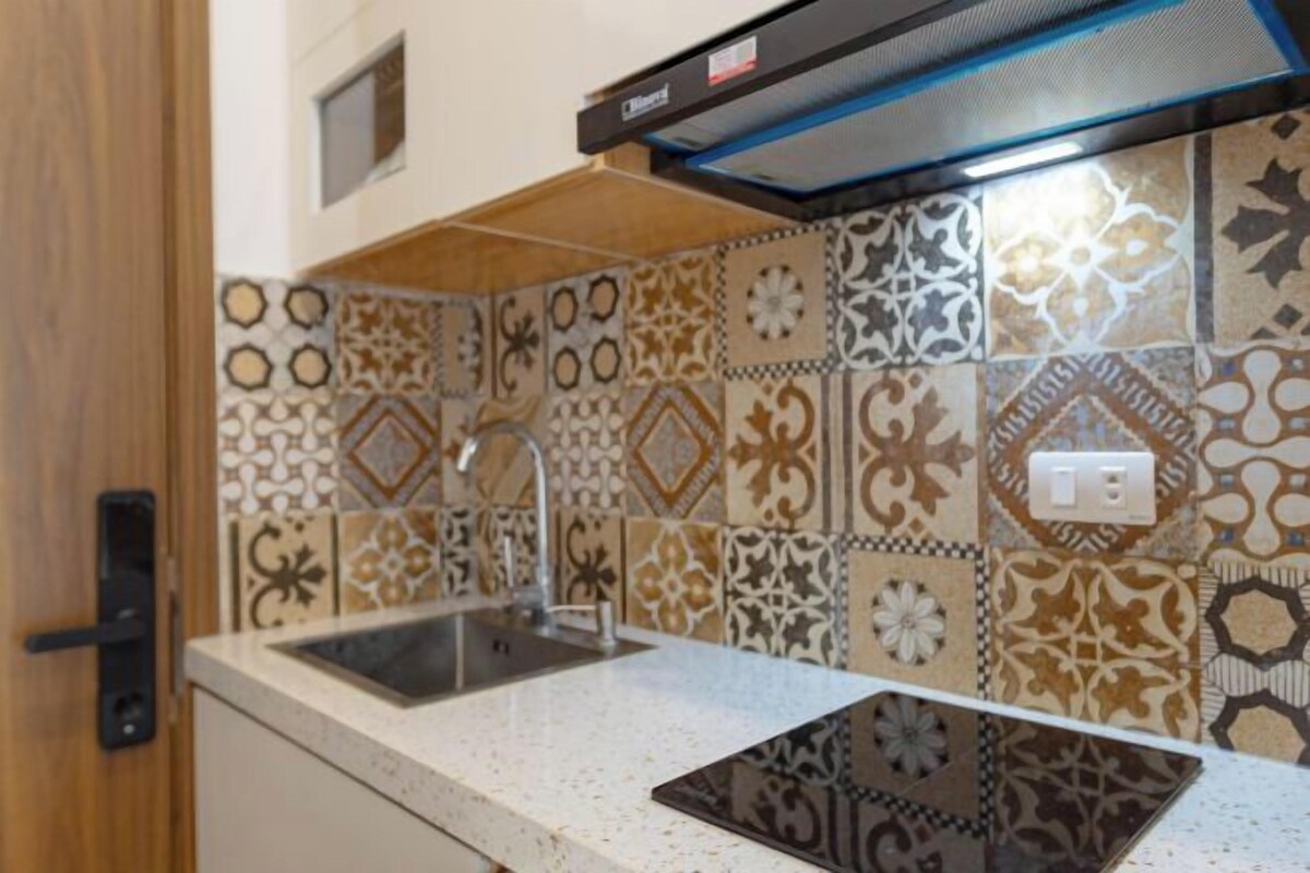 A kitchen with a patterned backsplash, a stainless steel sink, and a black range hood.