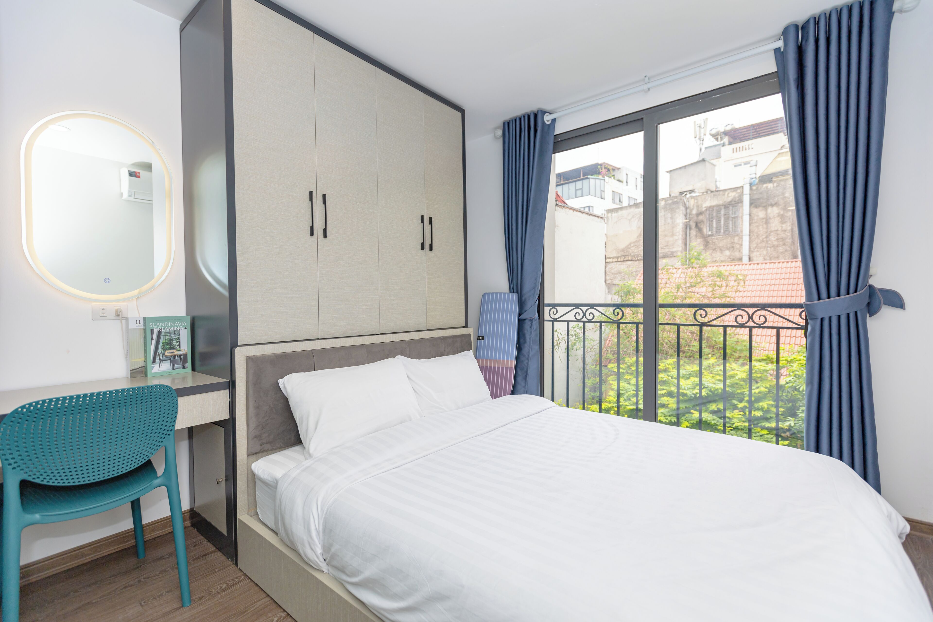 Un dormitorio con cama, escritorio, silla, armario y ventana con cortinas.