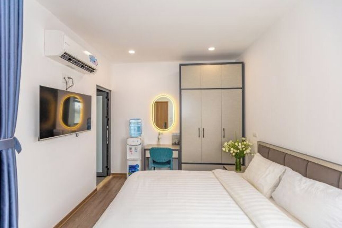 A hotel room with a bed, a desk, a chair, a wardrobe, a mirror, and a water dispenser.