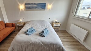 Une chambre à coucher avec un lit, un canapé orange, deux tables de chevet avec des lampes et un tableau au mur.