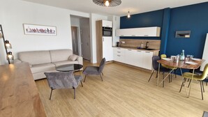 Un salon moderne comprenant un canapé, une table à manger avec des chaises, un coin cuisine avec des placards et un évier, ainsi qu’un mur d’accent bleu.