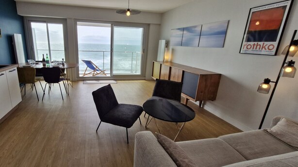 Un salon moderne comprenant un canapé, une table à manger avec des chaises, une petite table noire et un balcon avec un fauteuil.