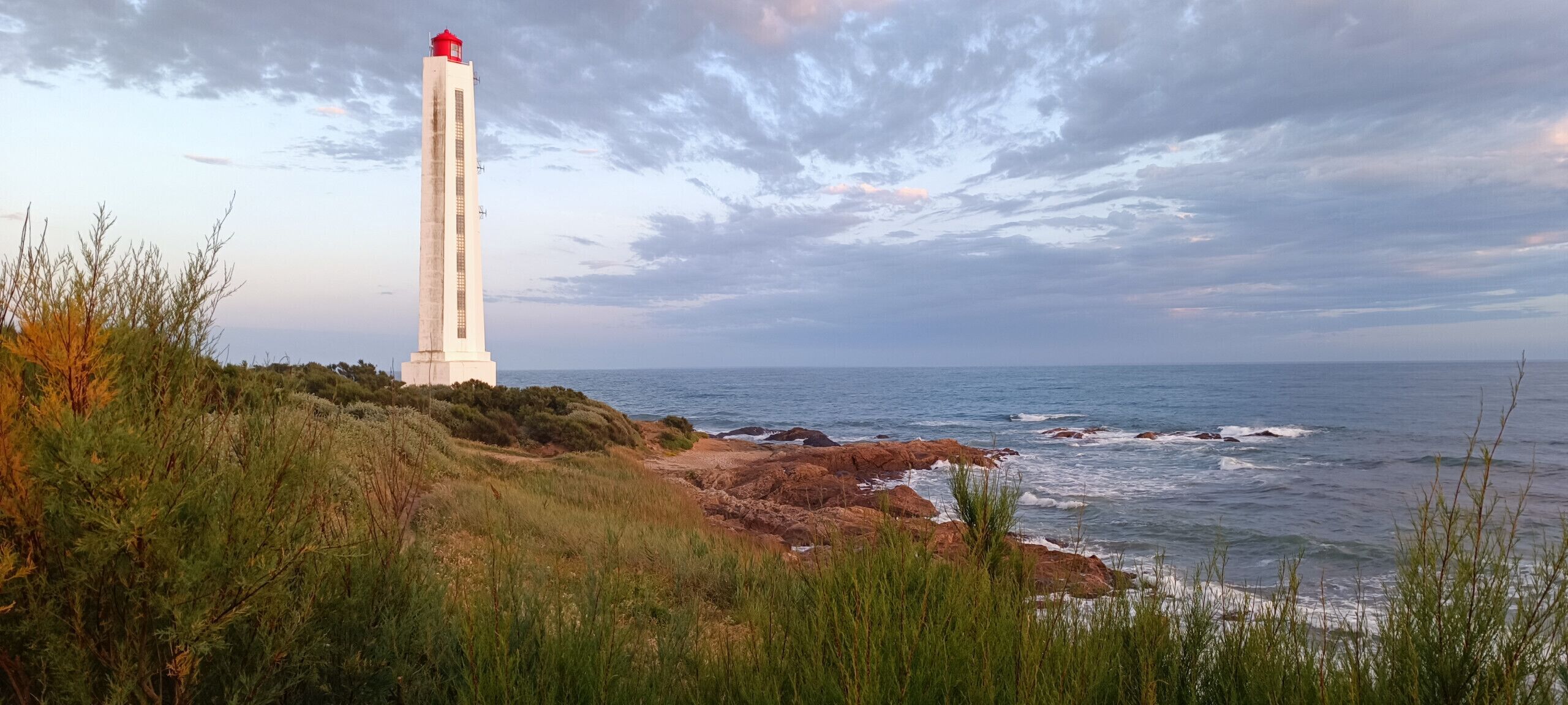 A coastal landscape with a lighthouse, rocky shoreline, and vegetation.