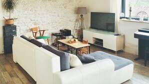 En stue med en stenvæg, en hvid sofa, et fjernsyn, en lampe og et vindue med udsigt.