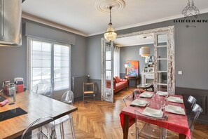 A dining area with a wooden table, chairs, and a chandelier. There is a red tablecloth on the dining table.