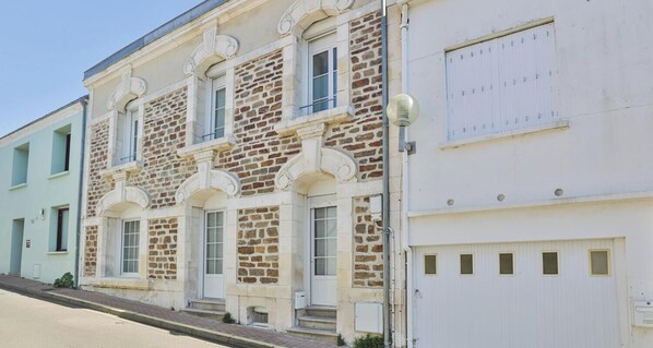 A multi-story building with stone facade, arched windows, and a white garage door. - Belle maison d'Armateur Sablais - 6 pers (Les Sables-d´Olonne)