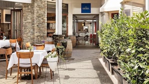An outdoor dining area with tables and chairs, a stone pillar, and a sign for 'The Sebel'. - Viaduct's Big Balcony Breathtaking Views (Auckland)