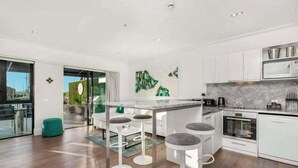 A modern kitchen with white cabinetry, a marble countertop, and a central island with bar stools. - Viaduct's Big Balcony Breathtaking Views (Auckland)