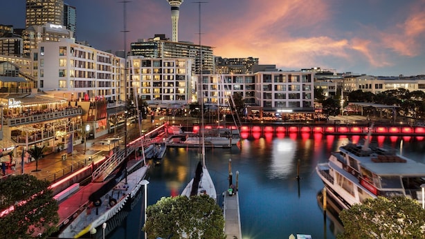 A waterfront hotel with multiple floors, a prominent tower, and a river with boats. - Viaduct's Big Balcony Breathtaking Views (Auckland)